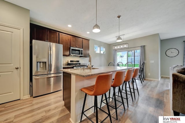 7237 Yankee Woods Dr, Lincoln, NE 68516 - kitchen with appliances with stainless steel finishes, light wood-style floors, a center island with sink, a breakfast bar area, and hanging light fixtures