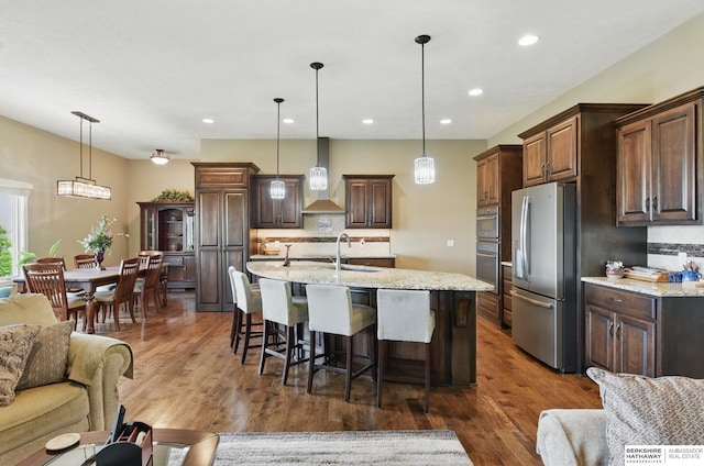 235 N 10th Ave, Springfield, NE 68059 - kitchen featuring appliances with stainless steel finishes, wall chimney range hood, backsplash, a breakfast bar, and recessed lighting
