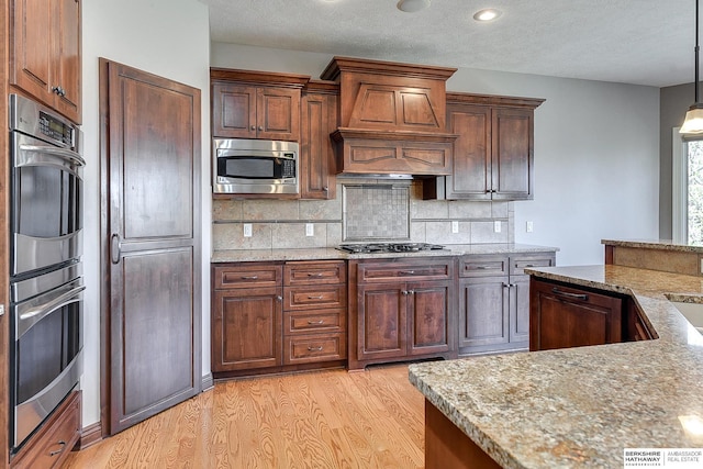 19252 Shirley St, Omaha, NE 68130 - kitchen with appliances with stainless steel finishes, light wood finished floors, backsplash, custom exhaust hood, and light stone countertops