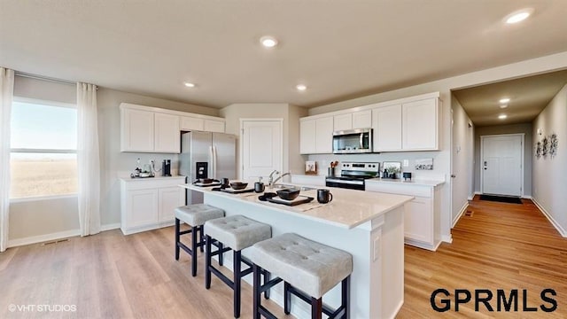 16401 Davidson St, Bennington, NE 68007 - kitchen featuring appliances with stainless steel finishes, a breakfast bar area, white cabinets, a kitchen island with sink, and light wood-style floors