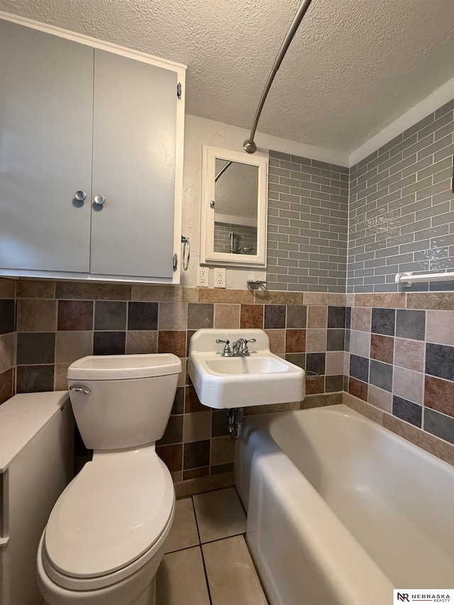 3836 Drexel St, Omaha, NE 68107 - bathroom featuring tile walls, toilet, a sink, a tub to relax in, and a textured ceiling