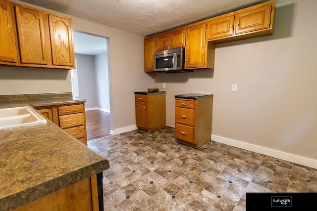 4518 Redick Ave, Omaha, NE 68152 - kitchen with stainless steel microwave, baseboards, brown cabinets, a textured ceiling, and a sink