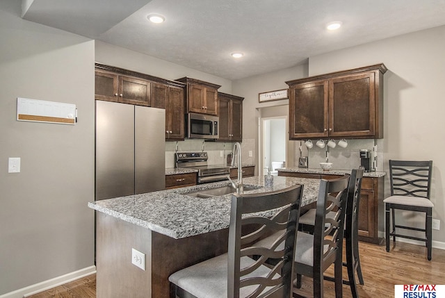 10202 N 152nd Ave, Bennington, NE 68007 - kitchen with stainless steel appliances, dark brown cabinets, backsplash, a breakfast bar area, and light wood-style flooring