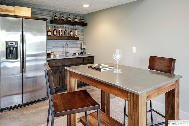 1611 S 208th St, Omaha, NE 68022 - kitchen with stainless steel refrigerator with ice dispenser, open shelves, light stone counters, a sink, and dark brown cabinets