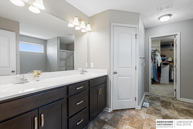 20904 Camden Ave, Omaha, NE 68022 - bathroom featuring a textured ceiling, double vanity, a shower stall, a walk in closet, and baseboards