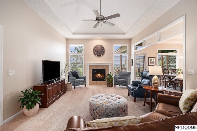 7409 N 160th St, Bennington, NE 68007 - living room with light colored carpet, a ceiling fan, a tray ceiling, a tiled fireplace, and baseboards