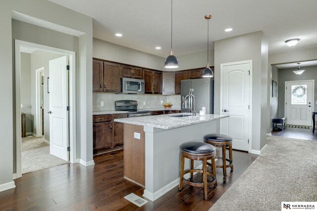 2206 Alexandra Rd, Papillion, NE 68133 - kitchen with appliances with stainless steel finishes, dark wood-style flooring, a kitchen island with sink, decorative light fixtures, and light stone countertops