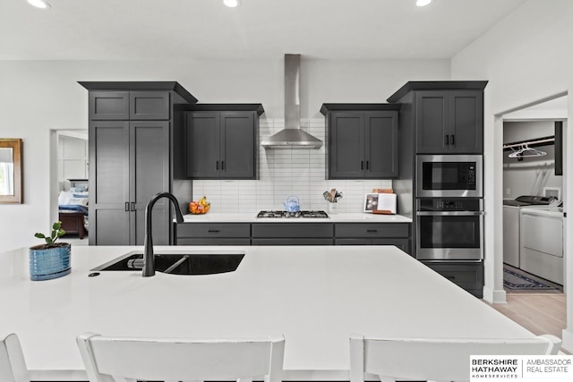 10317 S 191st Ave, Omaha, NE 68136 - kitchen with stainless steel appliances, washer and dryer, a sink, wall chimney range hood, and decorative backsplash