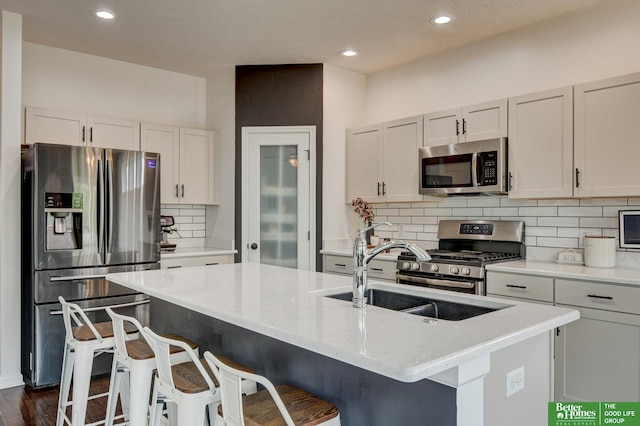 10505 Rosewater Pkwy, Bennington, NE 68007 - kitchen featuring appliances with stainless steel finishes, a sink, tasteful backsplash, a kitchen island with sink, and a kitchen bar