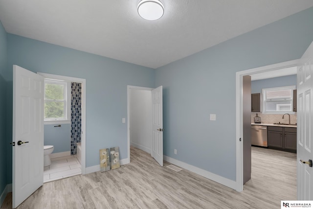2306 Ogden St, Omaha, NE 68110 - unfurnished bedroom featuring a sink, ensuite bathroom, multiple windows, and light wood finished floors