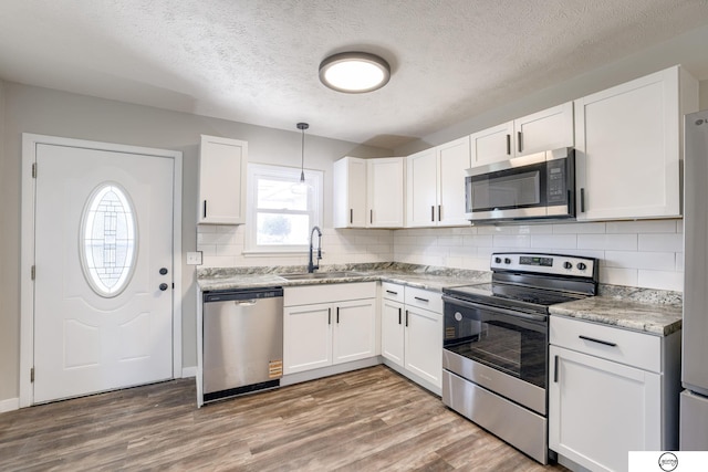 1801 Elk St, Beatrice, NE 68310 - kitchen with stainless steel appliances, a sink, white cabinets, wood finished floors, and decorative backsplash