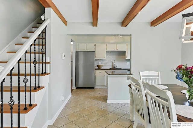 9704 Erskine St, Omaha, NE 68134 - kitchen with freestanding refrigerator, backsplash, beamed ceiling, light tile patterned floors, and white cabinetry
