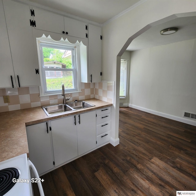 2134 S 48th St, Omaha, NE 68106 - kitchen with a sink, arched walkways, dark wood-type flooring, tasteful backsplash, and white cabinetry