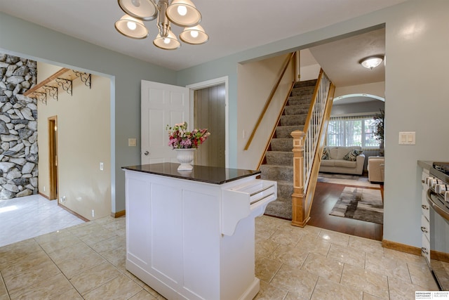 4459 F St, Omaha, NE 68107 - kitchen with arched walkways, a chandelier, dark countertops, a kitchen island, and white cabinetry
