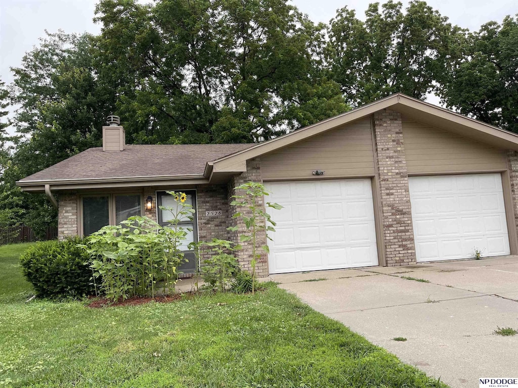 2528 Benson Gardens Blvd, Omaha, NE 68134 - view of front of property with brick siding, a chimney, a front yard, a shingled roof, and driveway