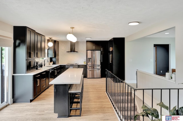 631 Overlook Ln, Beatrice, NE 68310 - kitchen with appliances with stainless steel finishes, wall chimney exhaust hood, a sink, light wood-type flooring, and hanging light fixtures