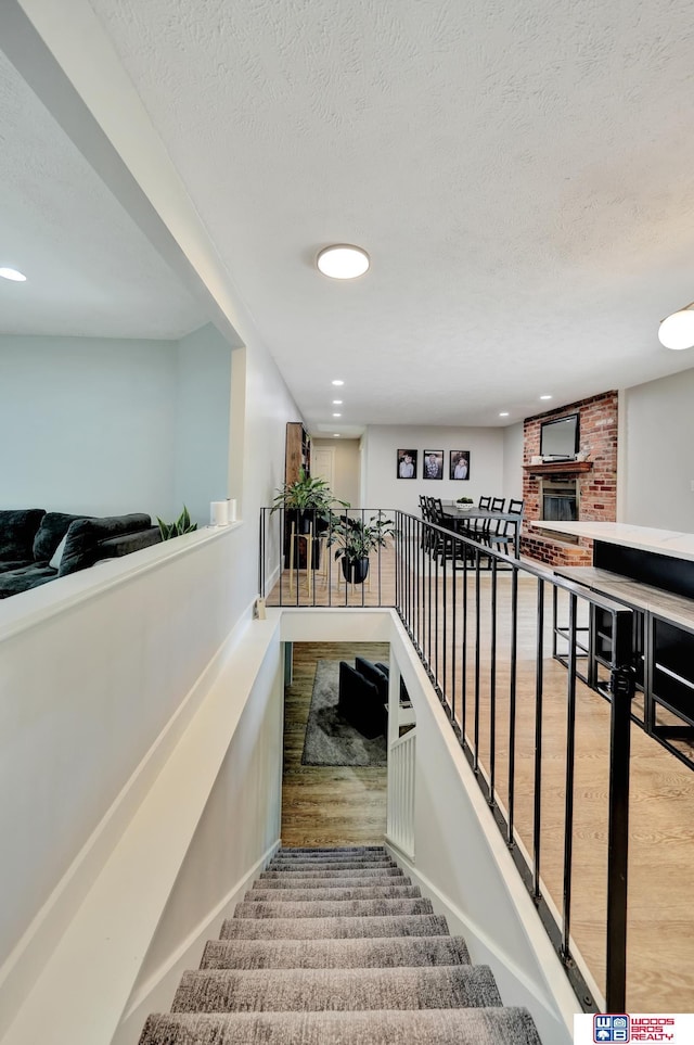 631 Overlook Ln, Beatrice, NE 68310 - staircase with baseboards, a brick fireplace, a textured ceiling, and recessed lighting
