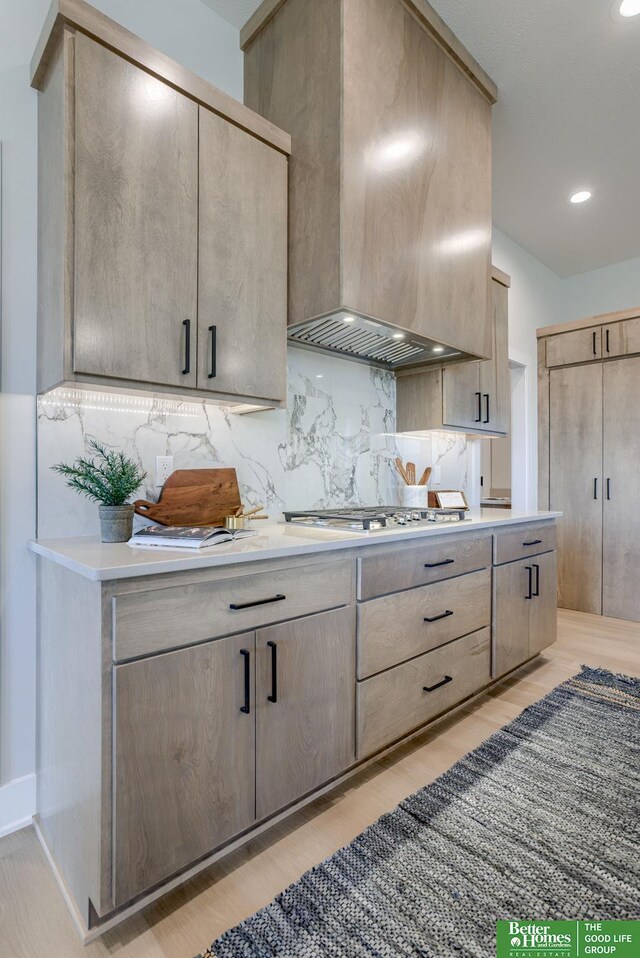 21056 Joseph St, Elkhorn, NE 68022 - kitchen with ventilation hood, light countertops, light wood finished floors, stainless steel gas stovetop, and backsplash