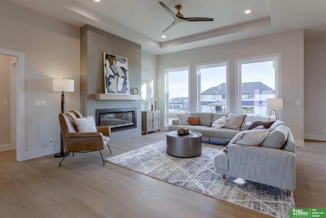 21056 Joseph St, Elkhorn, NE 68022 - living area with a tray ceiling, a glass covered fireplace, light wood-style floors, a ceiling fan, and baseboards