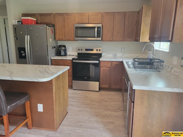 843 N 26th St, Beatrice, NE 68310 - kitchen featuring appliances with stainless steel finishes, light wood-style flooring, light countertops, brown cabinets, and a breakfast bar area
