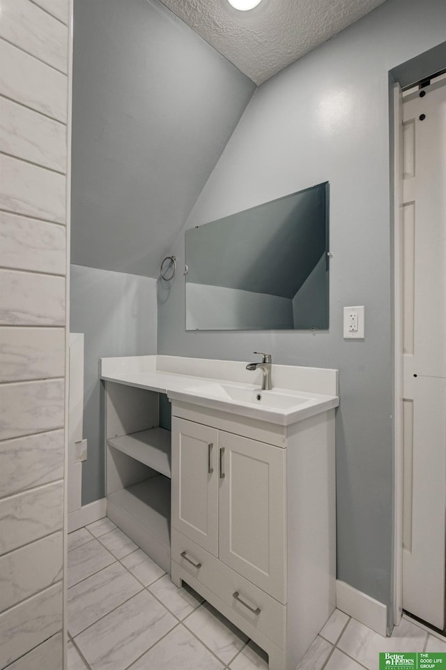 2864 Spaulding St, Omaha, NE 68111 - bathroom featuring vanity, a textured ceiling, vaulted ceiling, marble look tiles, and baseboards
