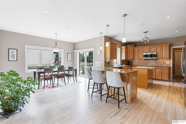 13303 Cuming St, Omaha, NE 68154 - kitchen featuring stainless steel microwave, light wood-style floors, decorative backsplash, a breakfast bar, and a sink