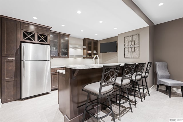 13303 Cuming St, Omaha, NE 68154 - kitchen with freestanding refrigerator, a breakfast bar, recessed lighting, glass insert cabinets, and dark brown cabinetry