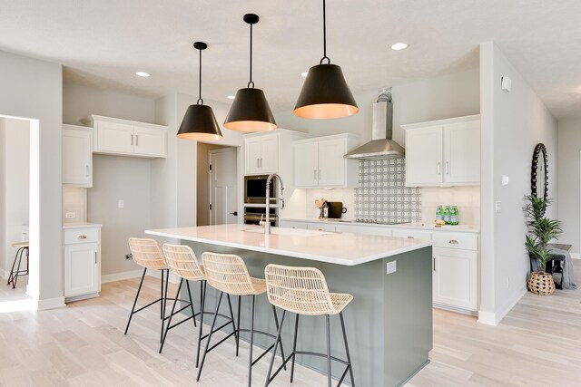 19920 Tyler St, Omaha, NE 68135 - kitchen with wall chimney exhaust hood, light wood-style flooring, decorative backsplash, an island with sink, and recessed lighting