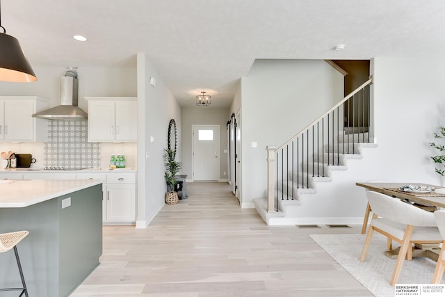 19920 Tyler St, Omaha, NE 68135 - kitchen featuring wall chimney range hood, light wood finished floors, light countertops, white cabinets, and recessed lighting