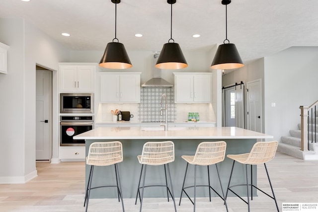 19920 Tyler St, Omaha, NE 68135 - kitchen with stainless steel appliances, wall chimney range hood, light wood-style floors, an island with sink, and light countertops