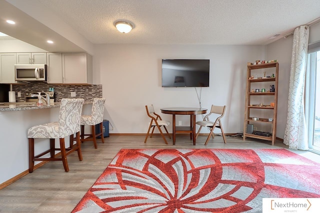 4115 N 45th Street Ct, Lincoln, NE 68504 - kitchen with stainless steel microwave, decorative backsplash, a textured ceiling, light wood finished floors, and a kitchen breakfast bar