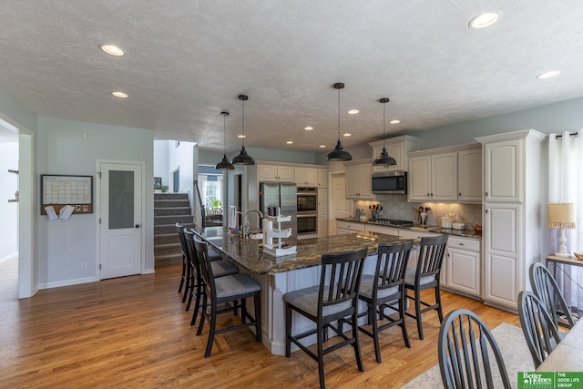 3902 Fox Ridge Dr, Bellevue, NE 68123 - kitchen featuring stainless steel appliances, a kitchen bar, decorative backsplash, light wood finished floors, and a textured ceiling