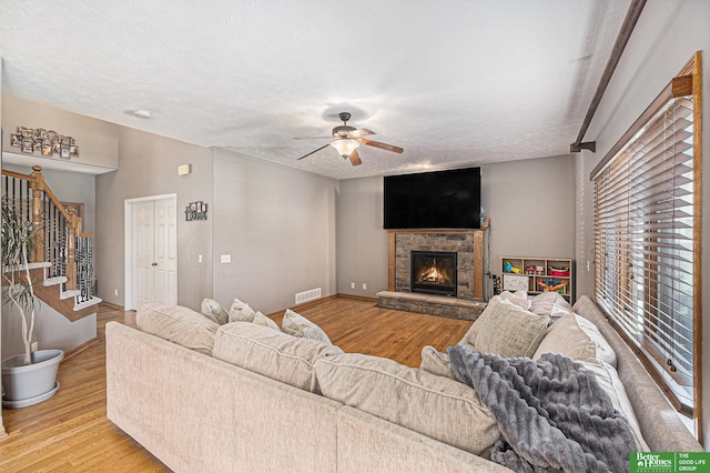 2231 Crystal Creek Dr, Papillion, NE 68046 - living room featuring wood finished floors, stairs, a stone fireplace, ceiling fan, and a textured ceiling