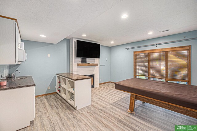 2231 Crystal Creek Dr, Papillion, NE 68046 - rec room featuring a sink, light wood-style flooring, baseboards, a textured ceiling, and a large fireplace