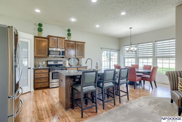 15930 Grebe St, Bennington, NE 68007 - kitchen featuring appliances with stainless steel finishes, a breakfast bar area, a center island with sink, light wood-style floors, and a textured ceiling