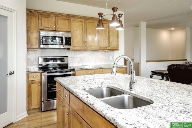 2627 N 166th St, Omaha, NE 68116 - kitchen featuring stainless steel appliances, a sink, light wood-style floors, light stone countertops, and decorative light fixtures