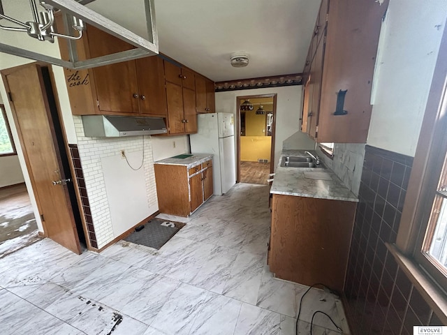 5329 N 47th St, Omaha, NE 68104 - kitchen featuring under cabinet range hood, brown cabinetry, freestanding refrigerator, light countertops, and a sink