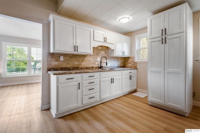1444 S 16th St, Omaha, NE 68108 - kitchen with light wood finished floors, white cabinetry, baseboards, tasteful backsplash, and a sink
