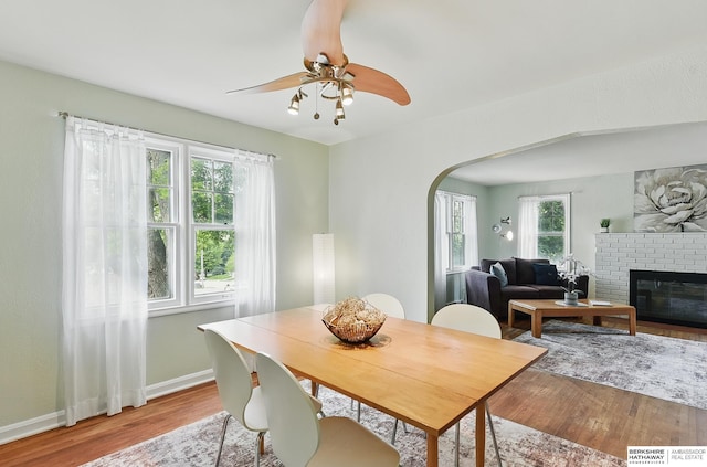 1511 S 60th St, Omaha, NE 68106 - dining area featuring arched walkways, wood finished floors, baseboards, a ceiling fan, and a brick fireplace