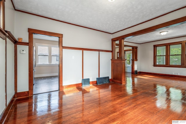 620 Dorcas St, Omaha, NE 68108 - unfurnished living room featuring a textured ceiling, ornamental molding, wood finished floors, baseboards, and decorative columns