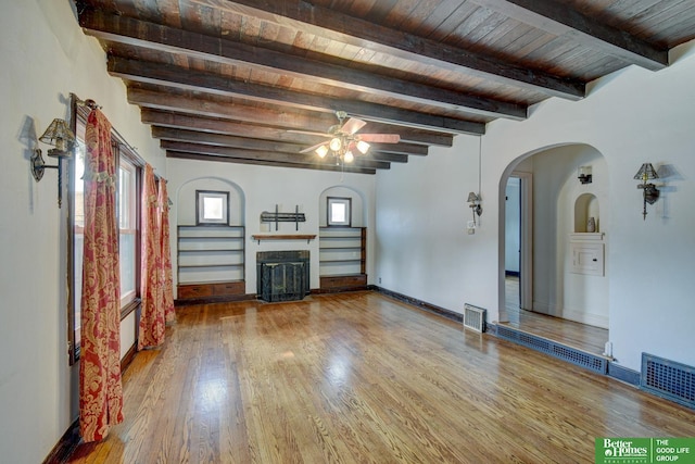 902 S 57th St, Omaha, NE 68106 - unfurnished living room featuring wood finished floors, a fireplace, arched walkways, a wooden ceiling with exposed beams, and a ceiling fan