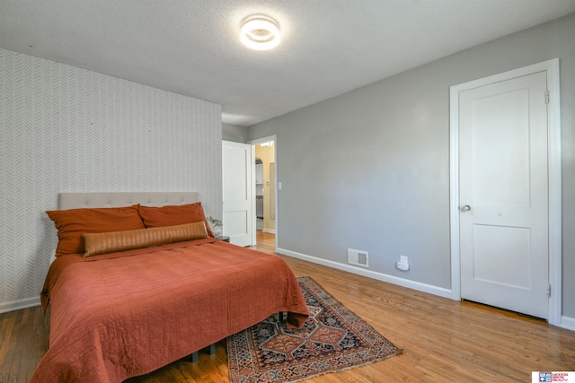 920 Clark Ave, Lincoln, NE 68510 - bedroom with wallpapered walls, baseboards, an accent wall, wood finished floors, and a textured ceiling