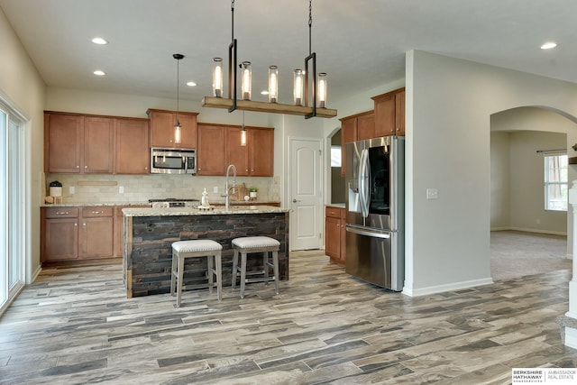 18337 Polk St, Omaha, NE 68135 - kitchen featuring appliances with stainless steel finishes, arched walkways, brown cabinetry, light wood finished floors, and recessed lighting
