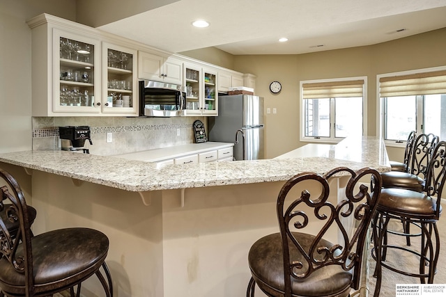 12829 Izard St, Omaha, NE 68154 - kitchen featuring appliances with stainless steel finishes, tasteful backsplash, a breakfast bar, a peninsula, and glass insert cabinets