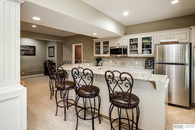 12829 Izard St, Omaha, NE 68154 - kitchen featuring appliances with stainless steel finishes, recessed lighting, glass insert cabinets, a breakfast bar, and backsplash