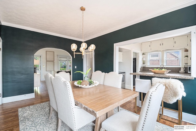 4427 Pine St, Omaha, NE 68105 - dining room featuring arched walkways, a chandelier, baseboards, ornamental molding, and wood finished floors
