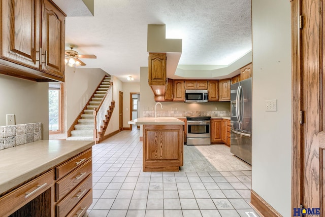 8240 Dorset Dr, Lincoln, NE 68510 - kitchen with stainless steel appliances, light tile patterned floors, a ceiling fan, light countertops, and brown cabinetry