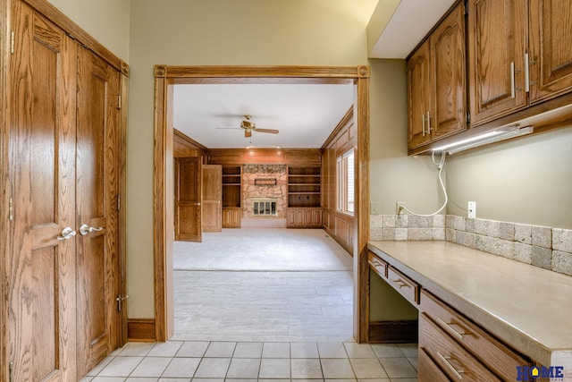 8240 Dorset Dr, Lincoln, NE 68510 - kitchen with ceiling fan, a stone fireplace, brown cabinetry, light countertops, and light tile patterned flooring