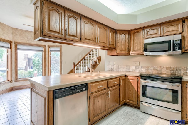 8240 Dorset Dr, Lincoln, NE 68510 - kitchen featuring appliances with stainless steel finishes, a sink, a peninsula, light countertops, and brown cabinetry