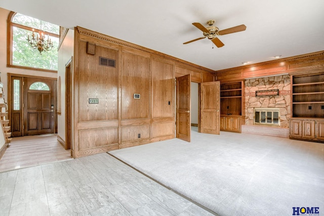 8240 Dorset Dr, Lincoln, NE 68510 - unfurnished living room featuring wooden walls, ceiling fan, built in features, a fireplace, and a chandelier